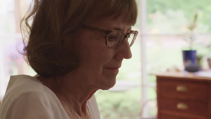 A woman with glasses in a room with plants and a window in the background
