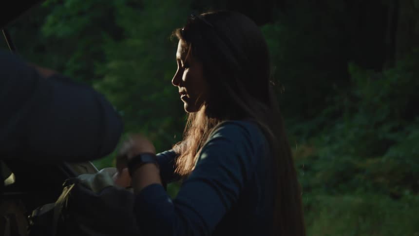 A man and woman unpack camping gear from the back of their vehicle