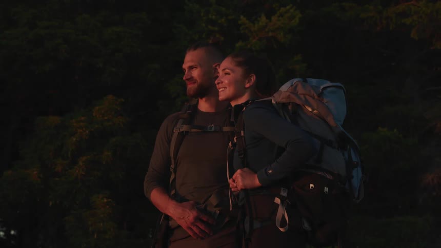 A man and a woman with backpacks standing with trees in the background