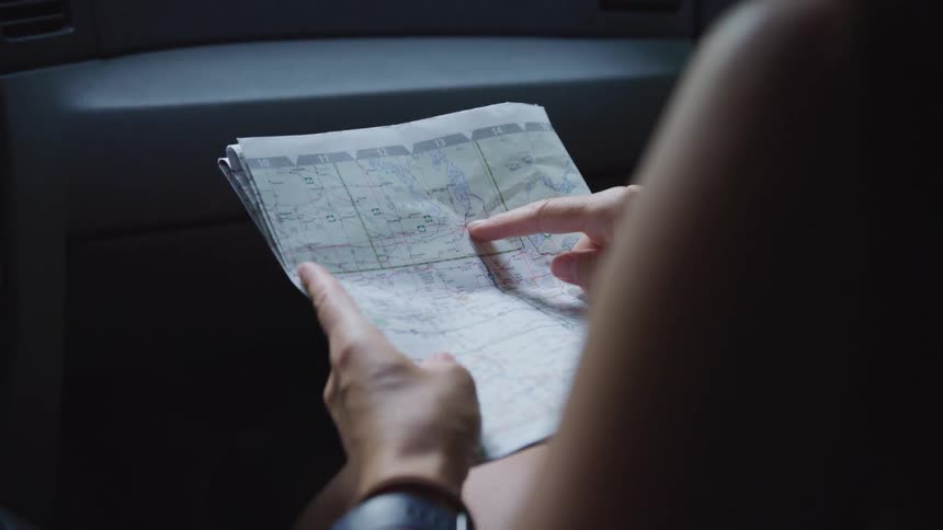 Person is holding a map with one hand and pointing to a location on the map with a finger on the other hand