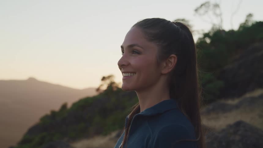 A woman smiles as she stands outside and looks out at the landscape