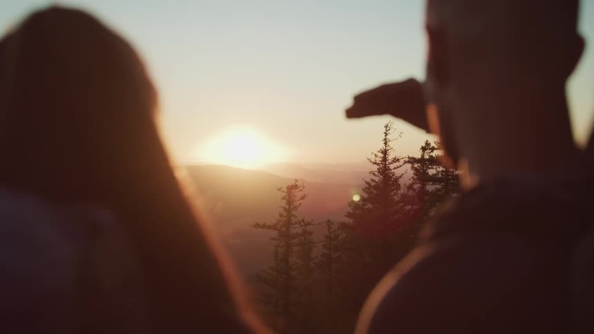 Silhouette of a couple looking at the golden sunset over the mountains