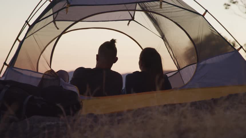 Couple lie in tent looking toward red tinted horizon