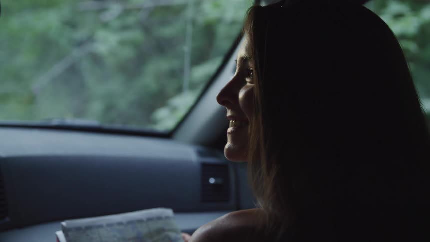 A female passenger smiling while holding a roadmap in a moving car
