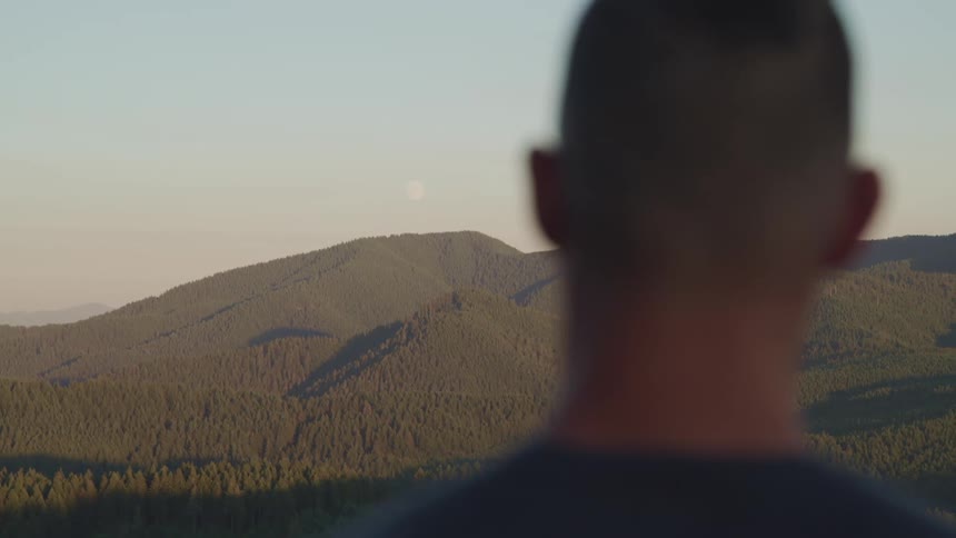 A man outside standing with hills trees the sky and clouds in the background