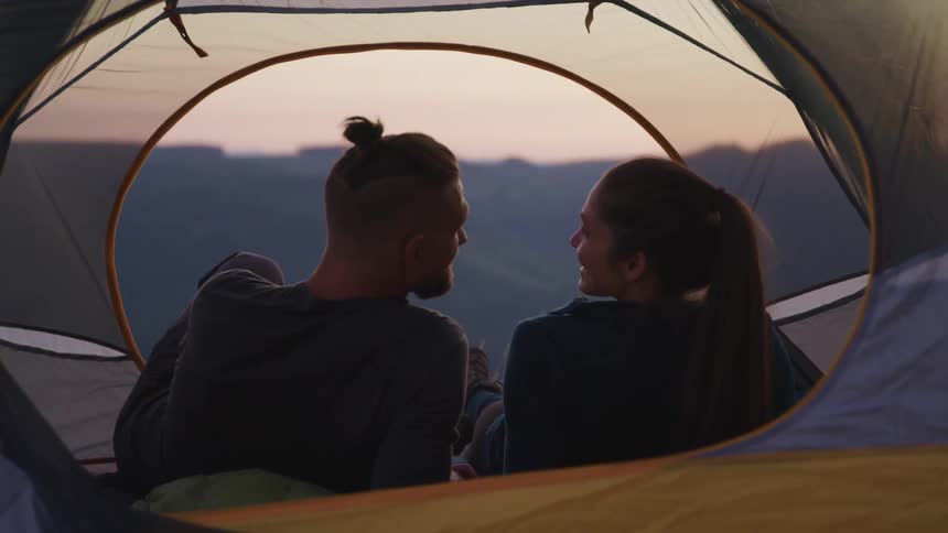 A man and woman sitting in a tent talk with one another