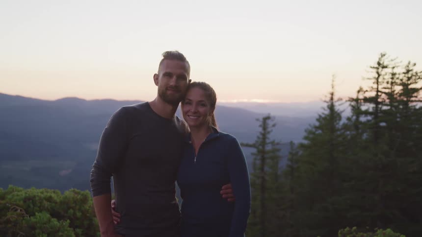 Young couple looking at the camera hugging by the waist in the mountains at sunset