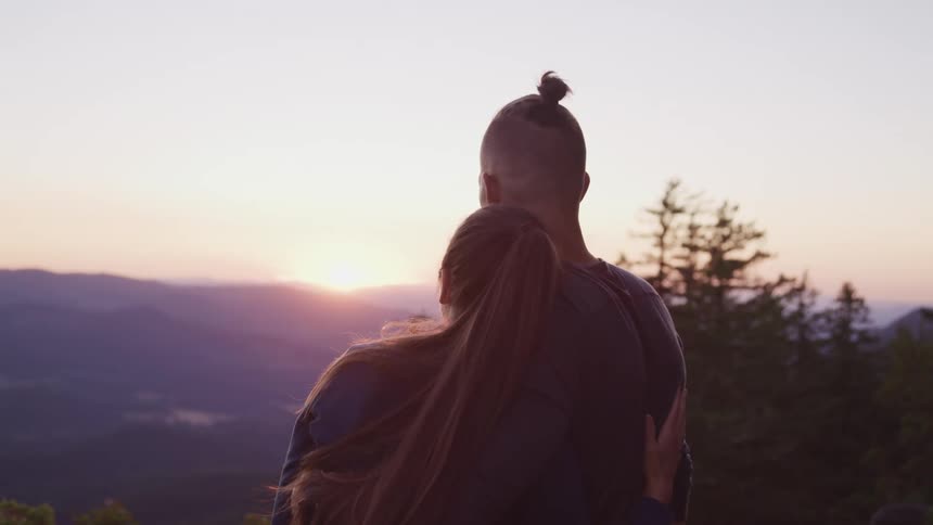 Young couple looking at the sunset atop a mountain