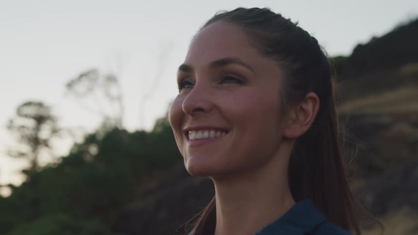 A young woman standing at the base of a hill smiles