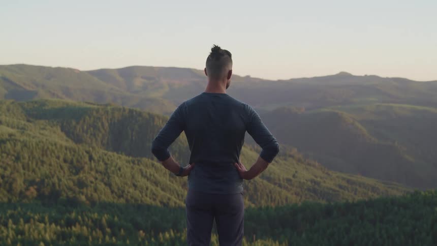 A man standing with trees hills the sky and clouds in the background