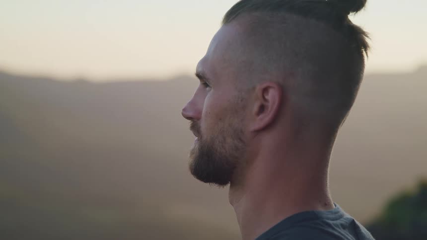 A man stands outdoors while he looks off in the distance with a thoughtful expression on his face