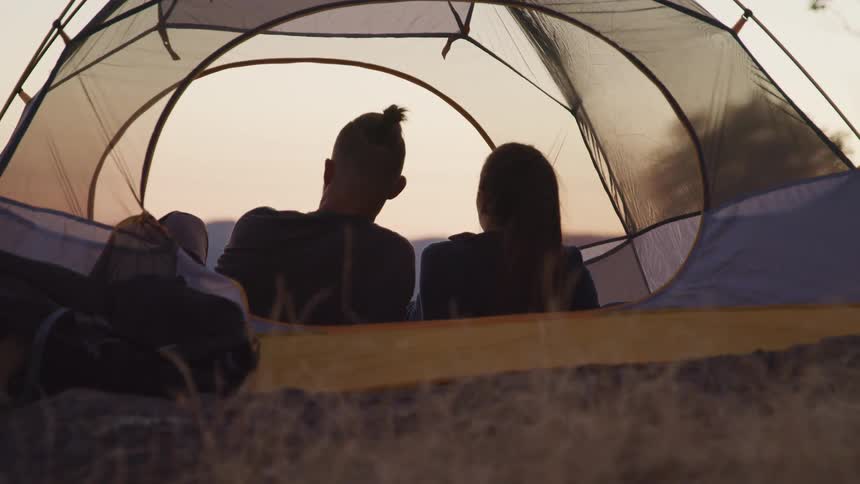 Man and woman lying in tent look toward red tinted horizon
