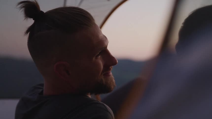 A man reclines within a tent outdoors and smiles at his female companion
