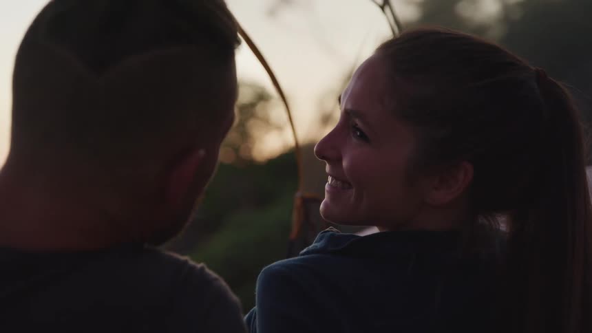 A man and woman sit outside and she looks at him and smiles