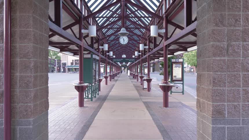 The walkway in the city is empty with a clock hanging in the middle