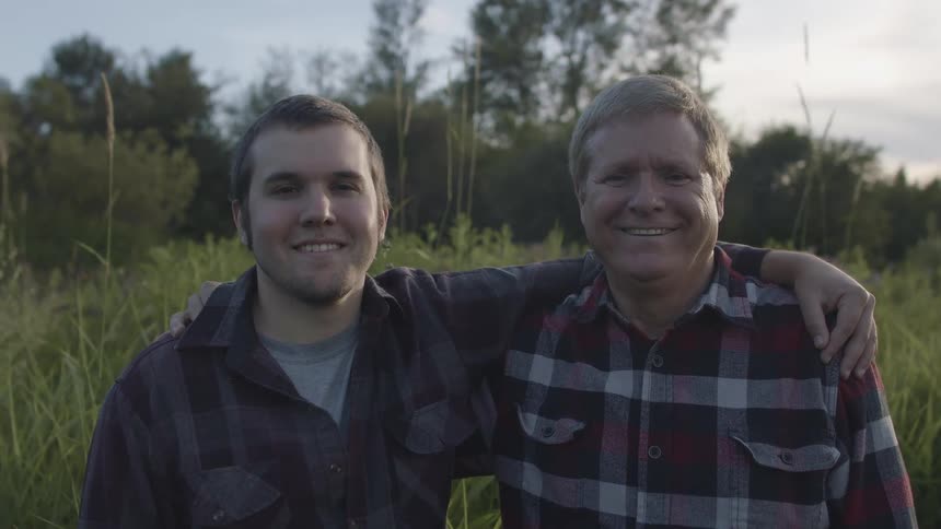 Father and son looking at the camera standing on a grass field at sunset