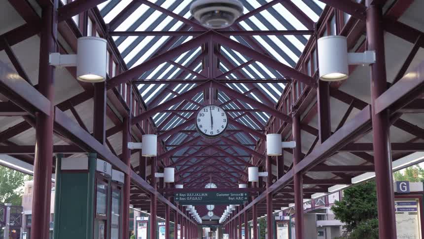 A clock hanging from a metal beam shows the time at a train station