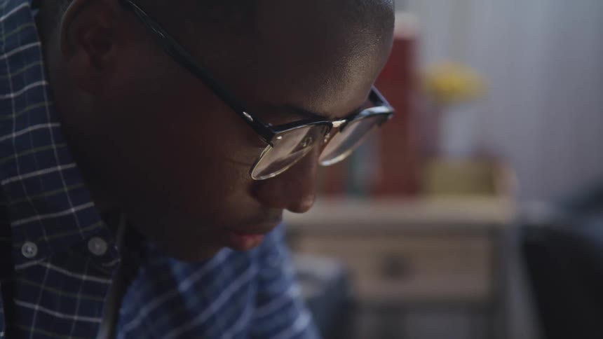 Black man with glasses and blue shirt looks down