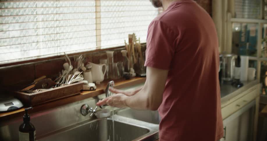 A man goes over to the sink and washes his hands