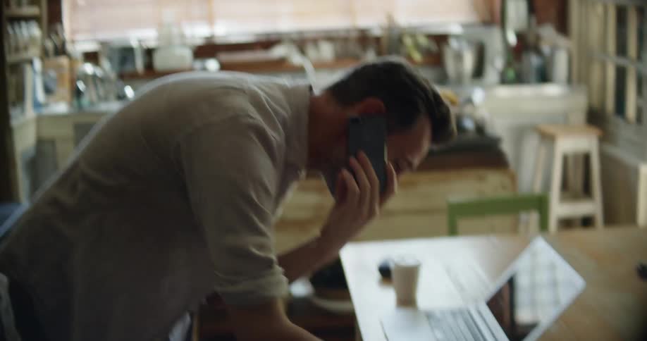 A man repeatedly shakes his head in frustration while on a phone call at home