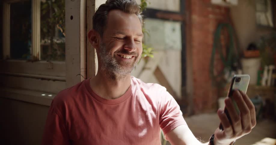 A white man takes a drink from a cup and then connects a visual call with someone on a smartphone