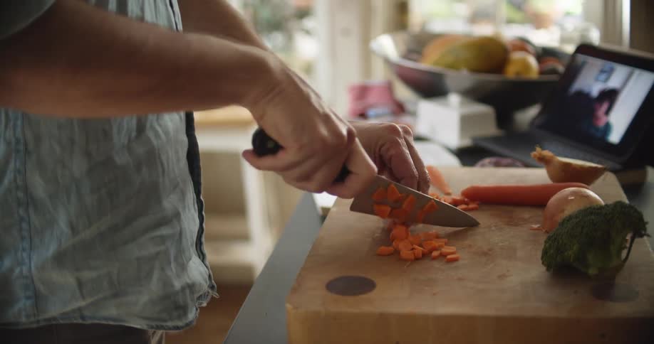 A man is video conferencing as he cuts up a carrot