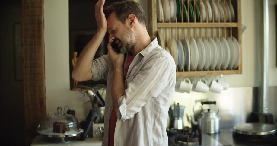A man is walking around his kitchen and talking on the phone