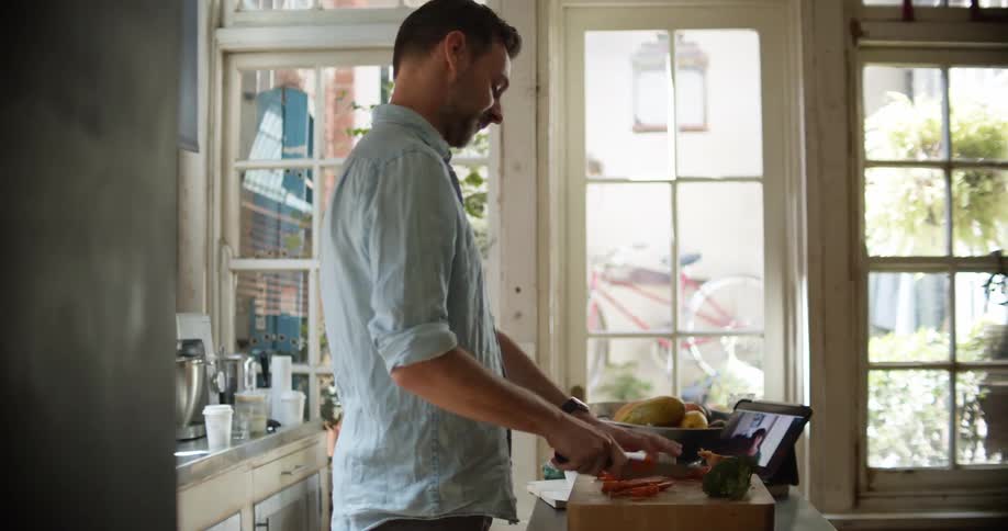 A man cooking at home video chats with someone on a laptop