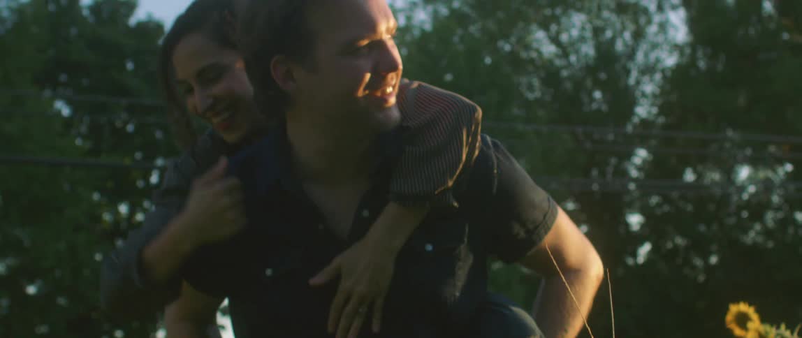 A woman jumps on her boyfriends back as they laugh in a field of sunflowers