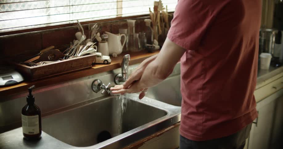 A white man washes his hands in a kitchen sink using pumped soap from a bottle