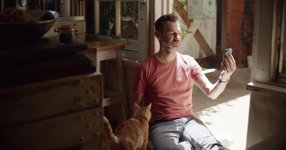 A man is sitting in his house and petting his cat