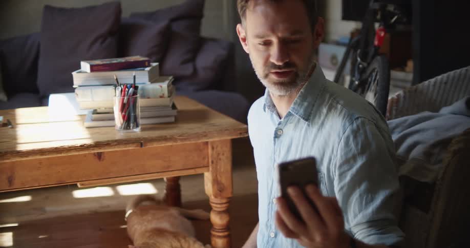 Man sitting in the floor of the living room shows his sleeping cat on a video call through a smartphone