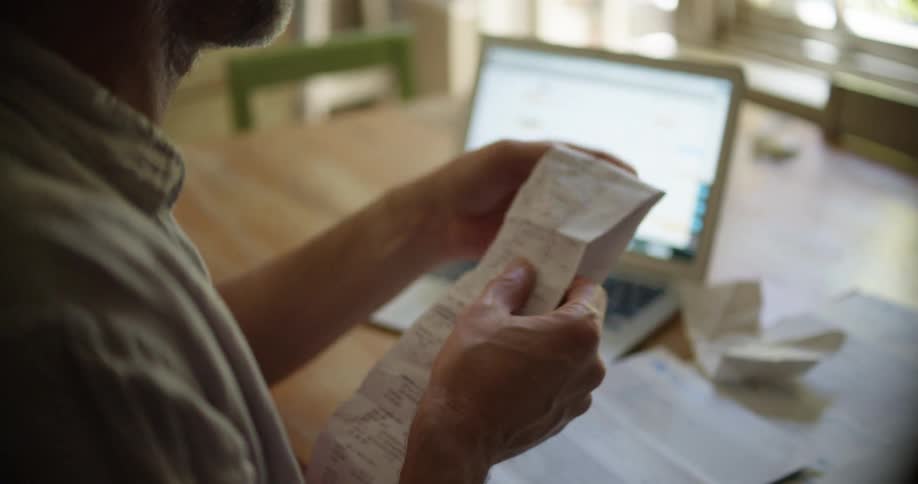 Tired man working from home files taxes on his laptop using a calculator