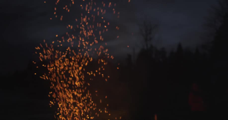 Sparks fly up into the night sky from a campfire