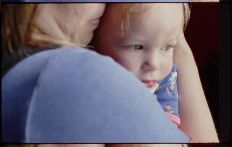 Mother lovingly holding baby girl in her arms close to her face in a room at home