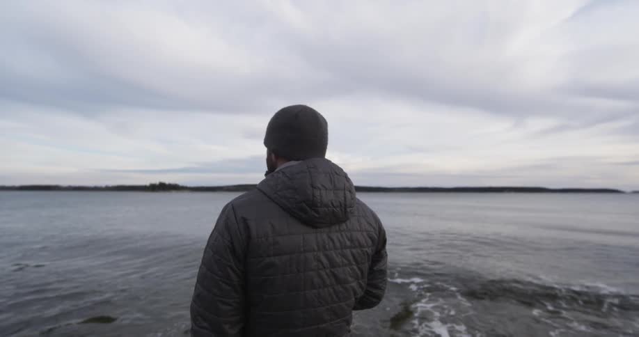 A man stands looking over the water