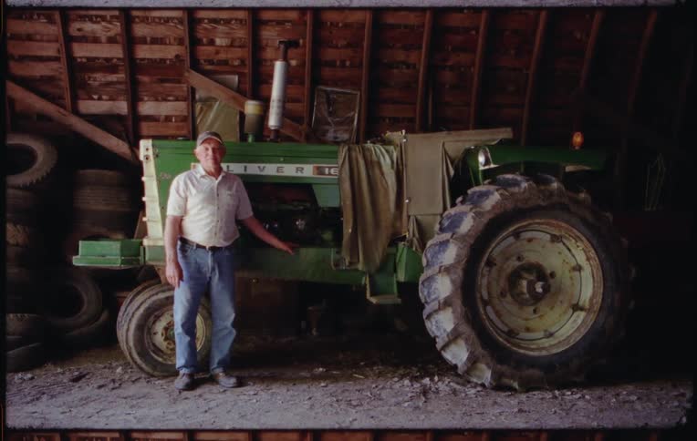 A farmer poses with one hand on his green tractor