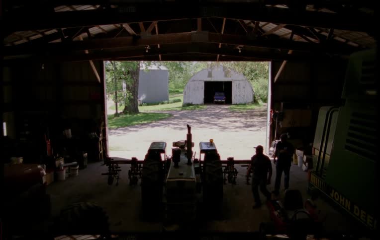 Two man open the doors of a barn in a farm to retrieve a tractor parked inside