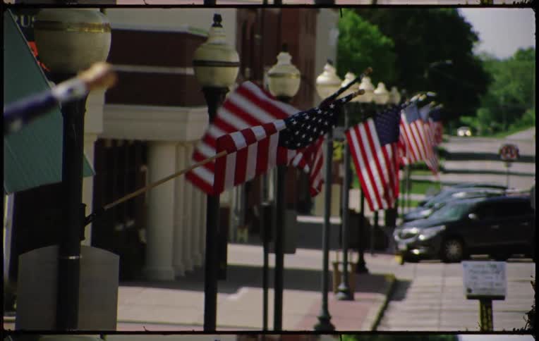 A row of american flags on street lights over a parking lot outside a building during the day