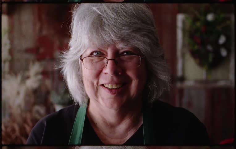 A woman with glasses in a room staring with a wall in the background