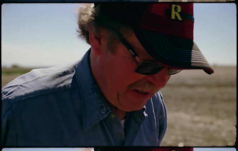 A man with a hat and sunglasses walking on a flat landscape with the sky and clouds in the background
