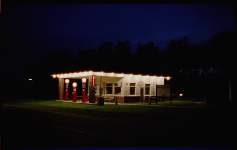 A vehicle drives past a closed business lit up brightly at night