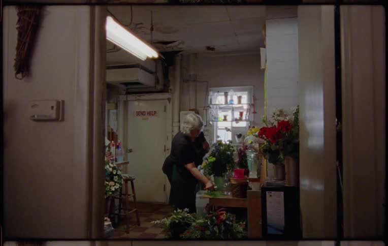 A woman with an apron in a room fixing a flower arrangement with a door in the background
