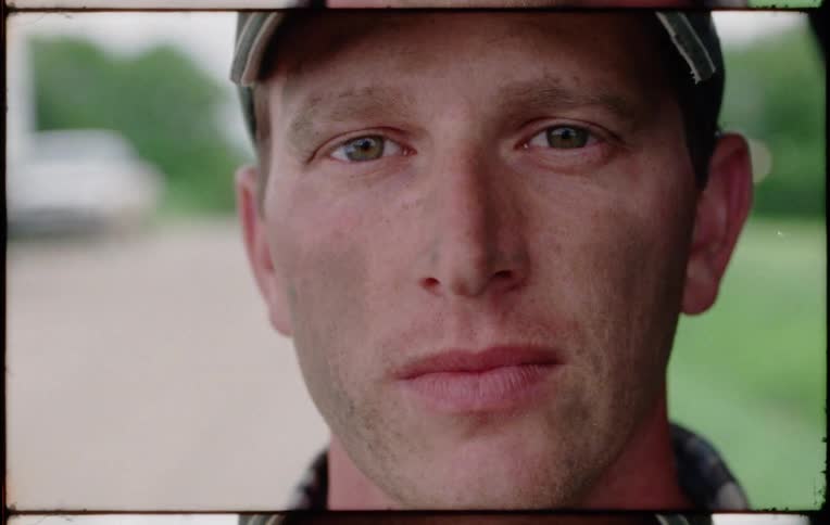 A man stares into the camera while standing outdoors during the day
