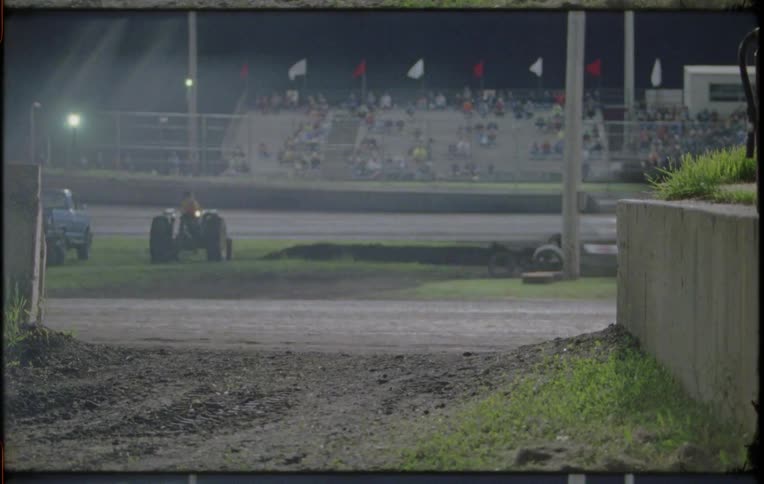 People sit in stands watching go carts race around a track at night