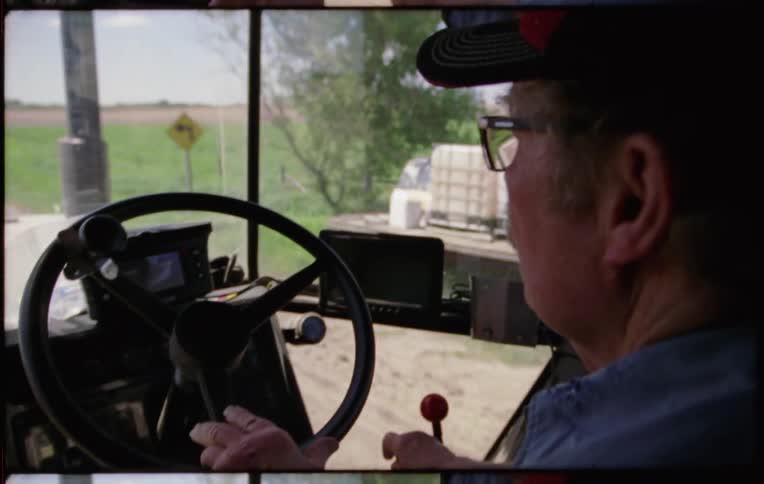Farmer driving a tractor over a dirt road through the farm at daytime