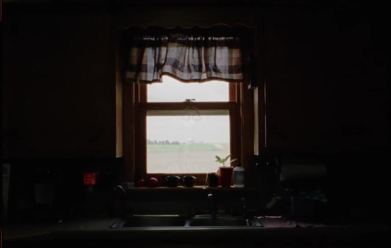 A kitchen with a sink and faucet dripping water with a wall and window in the background