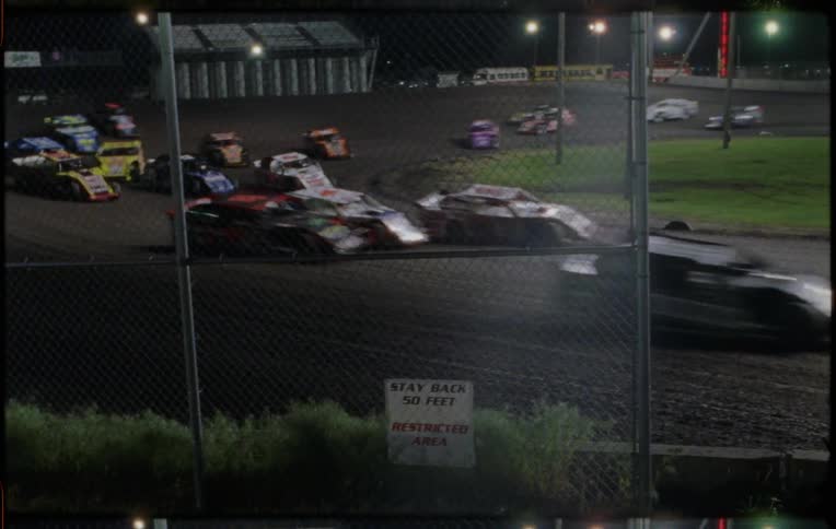 A racetrack with cars racing with streetlights trees and the sky in the background