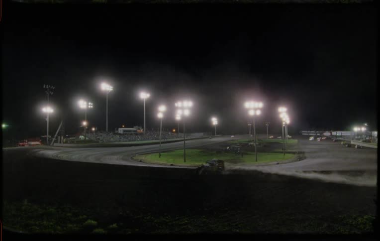 Dirt flies as vehicles race around a track at night