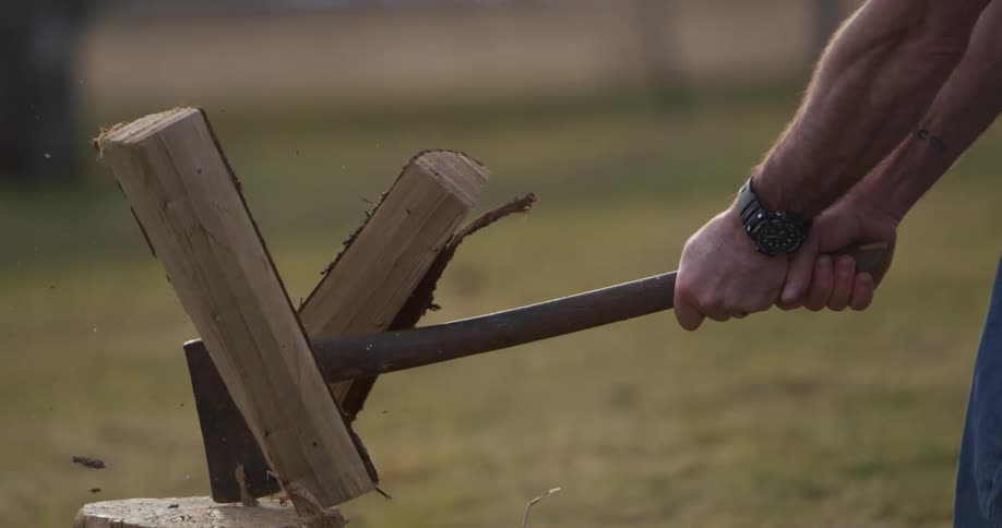 An axe comes down and splits a wood log